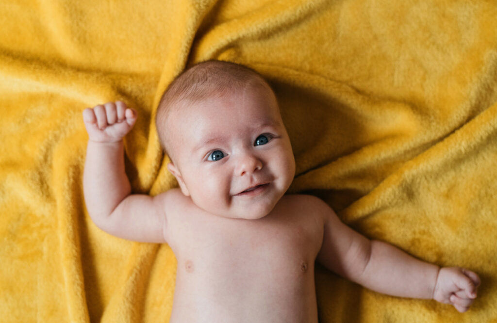 A baby on their back on a yellow blanket smiling