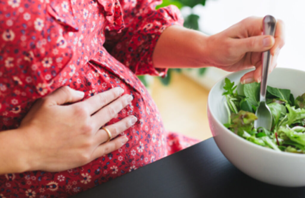 A pregnant woman touching her belly while eating a salad